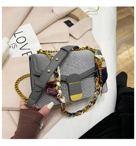 Dettaglio borsa grigia stampa coccodrillo con catena dorata e foulard di seta decorativo