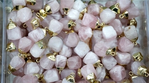 Close-up of bulk rose quartz stone pendants with gold-plated metal edges and loops