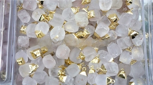 Macro view of raw clear quartz stone pendants with gold metal edge in a storage container