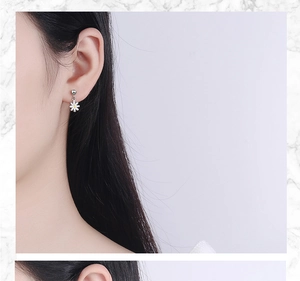 Close-up of a model wearing small white daisy stud earrings with silver details