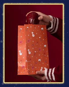 Putting a red apple into a Christmas paper gift bag with festive snowman illustrations