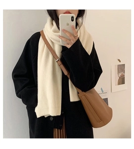 Close-up of a soft cream knit scarf styled with a black coat and brown bucket bag