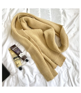 Flat lay of a warm yellow knit wool scarf with rib texture on white fabric backdrop