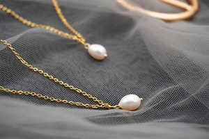 Close-up of dual gold link necklaces featuring elegant white teardrop freshwater pearls
