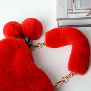 Detailed close-up of scarlet heart-shaped plush bag with fluffy poms and gold chain strap