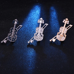Détail de broches en forme de violon et archet en or, argent et noir avec strass
