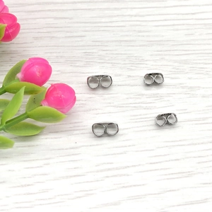 Close-up of four butterfly stainless steel earring backs on a wood background