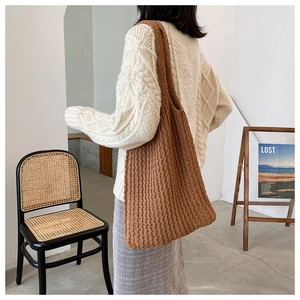 Detalle de un bolso tote de punto marrón con textura gruesa en el hombro del modelo