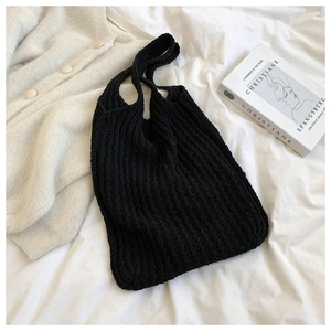 Detalle de la textura de punto de un bolso tote negro tejido sobre sábanas blancas con atrezo