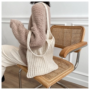 Modelo con un bolso tote de punto color crema en silla de mimbre para mostrar capacidad