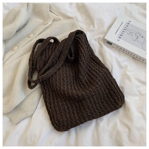 Detalle de bolso tote trenzado marrón oscuro con textura de punto sobre lino blanco