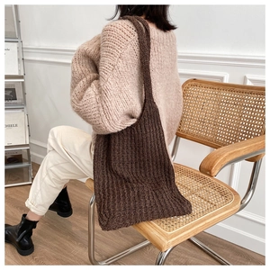 Detalle de un bolso tote de punto marrón oscuro llevado por una modelo en un interior