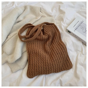 Vista plana de un bolso tote de punto marrón sobre sábanas blancas con un cárdigan beige