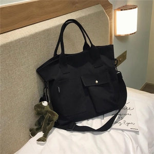 Detail shot of black canvas tote bag featuring front pockets and a cute frog charm