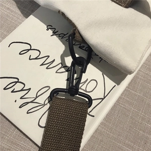 Macro detail of white canvas bag with brown woven strap and black matte metal hook