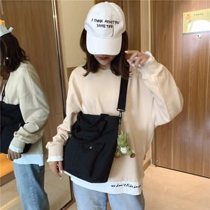 Detail of black canvas tote bag with dinosaur plush charm worn in a street style look