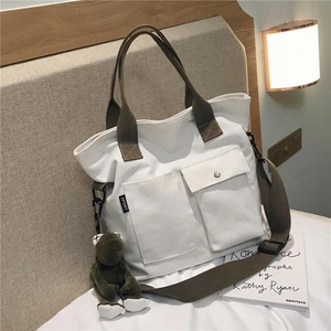 Close-up of white canvas tote with olive green straps and a plush frog pendant