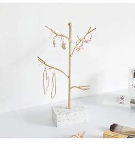 Macro view of golden metal jewelry tree on white terrazzo base with hanging earrings