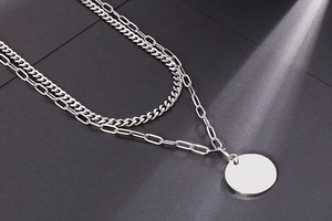 Detail of silver double-layered chain necklace with a blank round pendant on black background