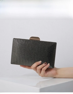 Close-up of black woven evening clutch bag with metallic clasp and glitter finish