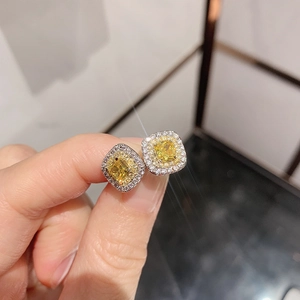 Close-up of square yellow gemstone earrings with sparkling white diamond halo on finger