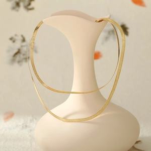 Detail of layered gold blade chains draped over a minimalist white art vase