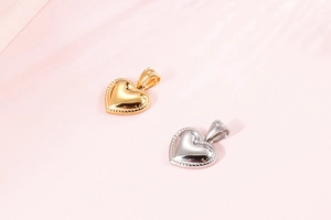Detail view of gold and silver heart pendants with beaded edges on pink water background