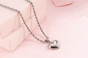 Macro shot of silver heart pendant with twist chain on a soft pink background