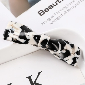 Detail of black and white marble acetate hair claw clip with bow design on a white tray