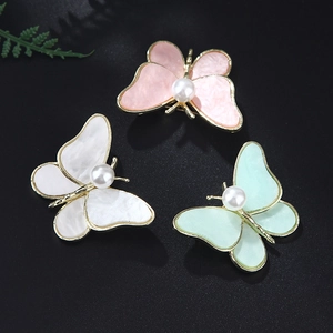 Detail of three pearl butterfly brooches in pink, white and green with gold metal frames