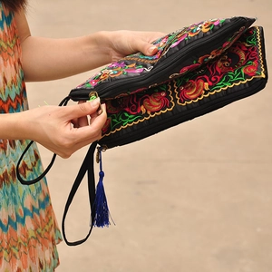 Close-up of black ethnic embroidery clutch with colorful silk floral patterns and blue tassel