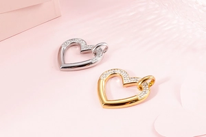 Détail de pendentifs coeur argentés et dorés sertis de cristaux sur fond rose
