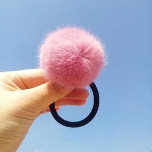 Pink plush mink fur pom pom hair tie with black elastic band against a blue sky