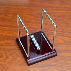 Newton's cradle with five silver metal balls and a dark brown wooden base on desk