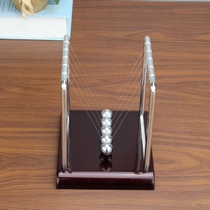 Detailed close-up of Newton's cradle with five metal balls on a wooden office desk