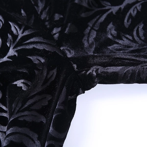 Close-up of black velvet flared trousers with intricate embossed floral texture and stitching