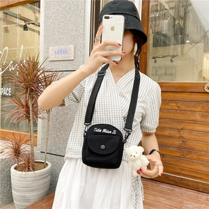 Close-up of black canvas crossbody bag with letter embroidery and cute plush bear charm