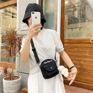 Close-up of black canvas crossbody bag featuring a cute white plush bear charm