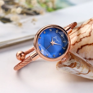 Detail view of rose gold rope-twist bangle watch with a blue faceted glass dial and crystals