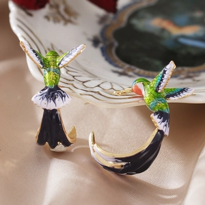Macro shot of colorful enamel hummingbird earrings with gold accents on silk fabric