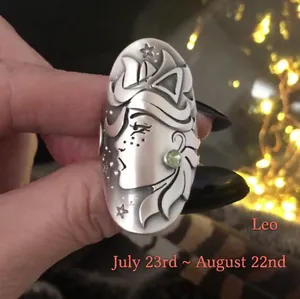 Detail of silver Leo zodiac ring featuring a matte floral face and green gemstone