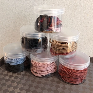 Six jars of colorful elastic hair ties stacked neatly on a checkered mat surface
