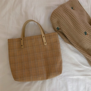 Detail of vintage brown plaid tote bag featuring leather handles and gold rivets