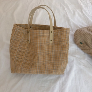 Detail of tan checkered tote bag with cream leather handles and metal rivet accents