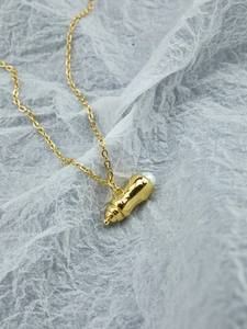 Vue macro d'un pendentif biberon doré avec perle blanche sur une chaîne minimaliste