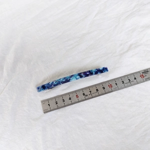 Detail showing a 10.5cm acetate hair clip with blue marble pattern beside a metal ruler
