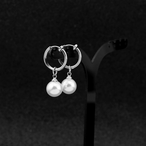 Detail of polished stainless steel earrings with elegant white faux pearl pendants on black