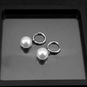 Detailed view of silver hoop earrings with white pearls on a black display tray