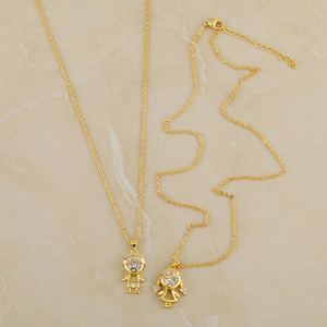 Gold-plated boy and girl pendant necklaces set with round cubic zirconia on marble background