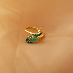 Detail of gold peacock ring featuring green oval gemstone and blue enamel feathers
